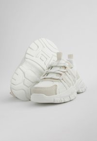 Pantofi sport albi și bej, realizați din plasă și materiale sintetice. Au o talpă texturată, design cu șireturi și călcâi amortizat.