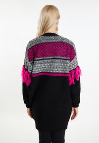 Juodas megztas per didelis megztinis, su tekstūruotu daugiakampiu dizainu, rožinėmis akcentais ir frizūromis ant rankovių.