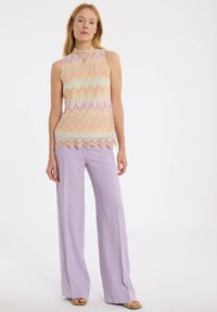 Ärmelloses Strickoberteil mit einem Zickzackmuster in Pastellfarben, kombiniert mit helllila weiten Hosen.