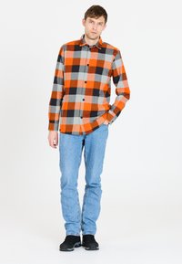 Herre langærmet skjorte i orange, grå og sort ternet mønster; knap-ned design med sorte knapper. Kombination med lyseblå jeans og sorte sko.