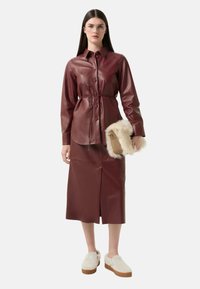 Bordeaux leren overhemdjurk met een tailleband, lange mouwen en een split aan de voorkant. Gecombineerd met crèmekleurige slippers en een clutch met een bontaccent.