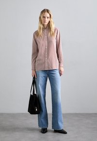 Camicia a righe rosse e bianche con colletto alto, abbinata a jeans flare azzurri chiari e una borsa tote nera.