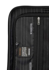 Interno di una borsa da viaggio nera con un compartimento con zip, caratterizzato da una texture in tessuto liscia, un motivo a righe bianche e un'etichetta con il marchio.