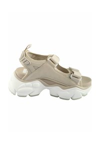 Sandales de sport beiges avec une épaisse semelle blanche, des brides réglables, un matériau supérieur lisse et un semelle intérieure texturée.