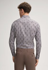 Langsleeve shirt met een grijs-wit bloemmotief, zachte stof, klassieke kraag en knoopsluiting aan de mouwen, gedragen met een paar bruine broeken.