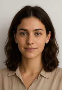 Ritratto di una donna con capelli castani mossi di media lunghezza. Indossa piccoli orecchini rotondi in argento e una camicia beige con colletto. Sfondo semplice.