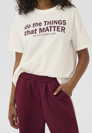 Biała bawełniana koszulka z bordowym napisem "do the THINGS that MATTER" oraz "stay chill and drink coffee." W połączeniu z bordowymi dresami.