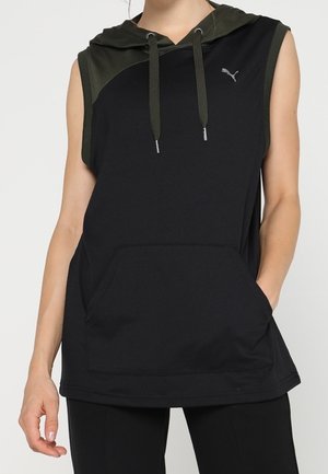 Sweat à capuche noir sans manches avec capuche et cordons de serrage vert foncé, poche kangourou à l'avant, porté avec un pantalon noir.