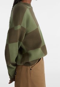 Grön tröja med stort rutmönster, med rund halsringning, sänkta axlar och ribbad nederkant. Mjuk textur, avslappnad passform.