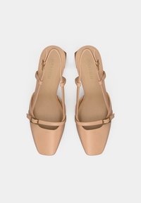 Sandales à talons carrés couleur nude avec une finition brillante, dotées d'une bride unique à la cheville avec une boucle métallique et des découpes sur les côtés.