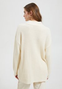 Crème gebreide oversized trui met kraag, relaxte pasvorm en geribbelde manchetten, met een gestructureerd patroon en een langere achterzoom.