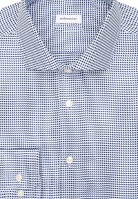 Camicia a maniche lunghe con bottoni, piegata, con un motivo geometrico blu e bianco e un'etichetta "seidensticker" visibile all'interno del colletto.