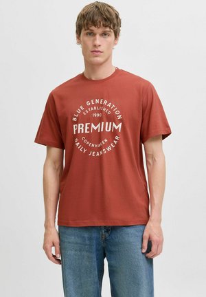 Rustrød t-shirt lavet af bomuld, med et cirkulært hvidt grafik med tekst og etableringsdato. Korte ærmer, afslappet pasform.
