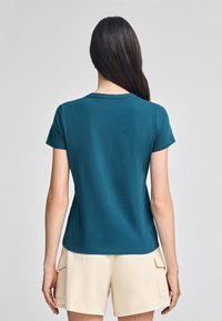 Teal t-shirt med kort ärm och rund halsringning, figurnära form och slät yta, tillsammans med ljusbeiga cargo shorts.