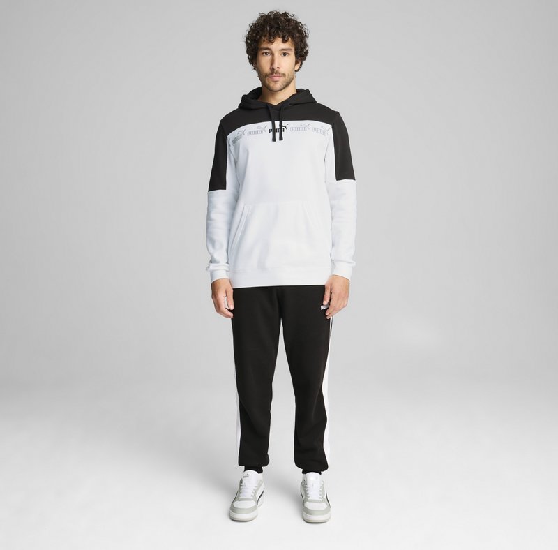 Sweat à capuche blanc avec accents noirs, doté d'une poche avant et d'une capuche à cordon, associé à un pantalon de jogging noir avec des bandes blanches sur les côtés. Fond gris.