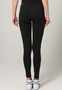 Černé legíny s těsným střihem, vyrobené z elastické látky, s pružným pasem, doplněné bílými teniskami.