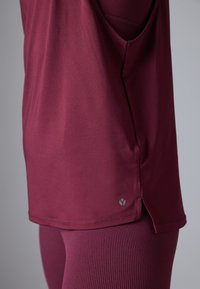 Burgundia sporditop, mis on valmistatud pehmest materjalist, ümarate äärtega, külgmiste lõhikute ja väikese logoga vasakul allservas.