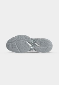 Semelle d'une chaussure de sport grise avec des motifs texturés et une section centrale transparente pour la flexibilité et l'adhérence.