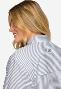 Camicia a righe con bottoni, con strisce blu e bianche sottili, dotata di colletto curvo e un patch logo sul retro. Tessuto di cotone, design informale.