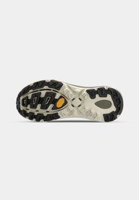 Trail running shoe outsole features a multi-directional lug pattern in black rubber with a cream midsole and Vibram detailing for grip.