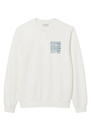 Felpa bianca in misto cotone, con una toppa rettangolare blu che presenta il logo "LACOSTE" ripetuto. Collo tondo standard e polsini a costine.