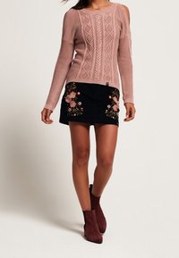 Helles rosa gestricktes Sweatshirt mit offenem Schulterdesign und Kabelmuster. Dunkelblauer Rock mit floralem Stickerei. Burgunderfarbene Stiefeletten.