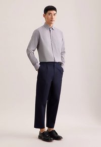 Lysegrå, ternet skjorte med knaplukning ved kraven kombineret med marineblå, skræddersyede bukser og sorte snøresko. Glat stof og struktureret pasform.