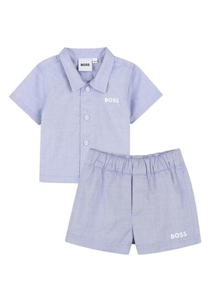 Completo con camicia azzurra a maniche corte con bottoni e pantaloncini con vita elastica, entrambi con il logo "BOSS" sul petto della camicia e sulla gamba dei pantaloncini.