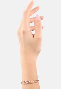 Pulsera de oro rosa con un símbolo de infinito, una mezcla de cuentas pálidas y una textura de cadena trenzada, que se lleva en una mano sobre un fondo claro.