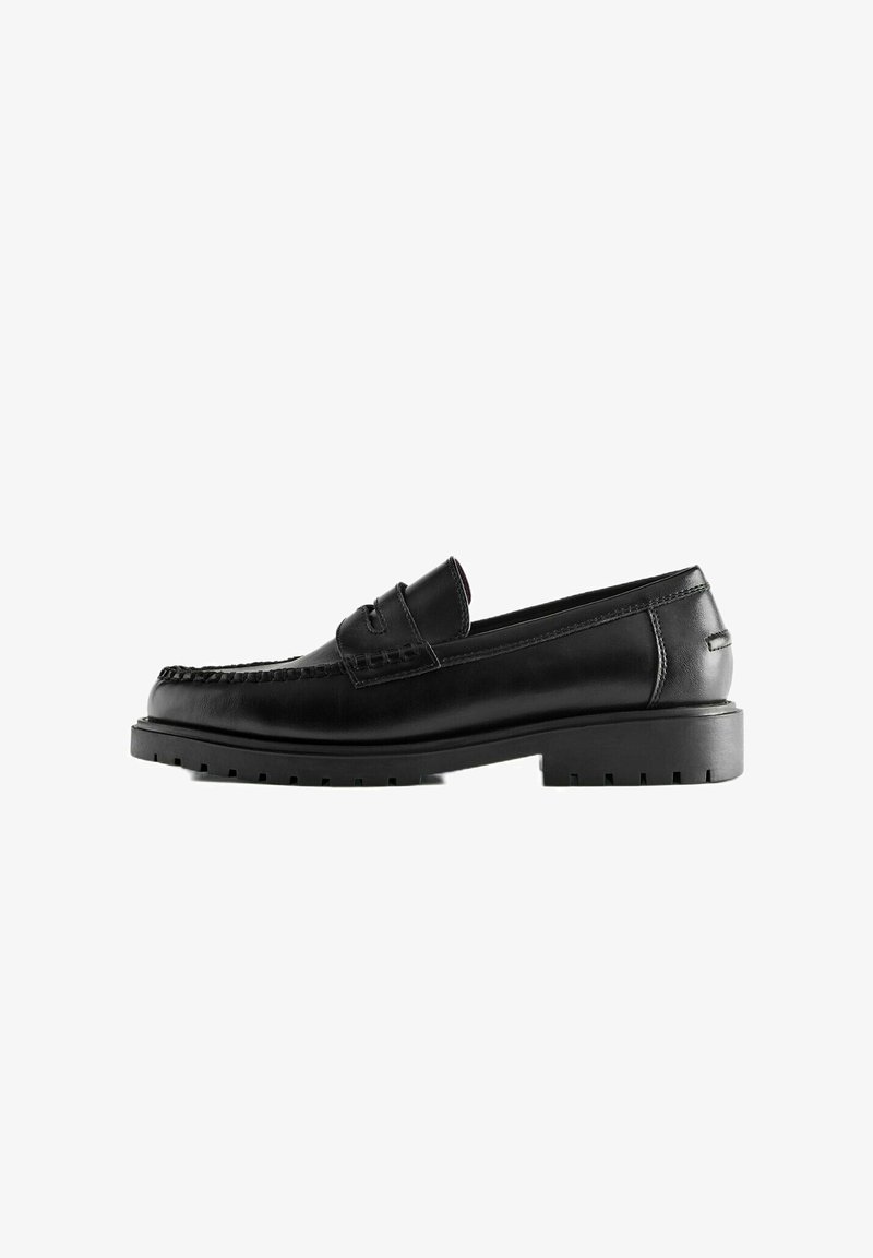 Mocassin noir en cuir avec semelle en caoutchouc épaisse et coutures mocassin, vue latérale sur fond blanc.