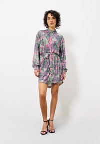 Kurzärmeliges Kleid mit Kragen, ausgestattet mit einem mehrfarbigen Blumenmuster auf strukturiertem Stoff, tailliert mit einem passenden Bindegürtel. Schwarze hohe Schuhe.