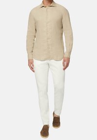 Camisa de lino color beige claro con mangas largas y botón frontal, combinada con pantalones blancos y zapatos de estilo slip-on marrones.