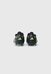 Black football cleats with a textured finish, featuring reflective accents and bright green details. Clear studs on the sole for traction.