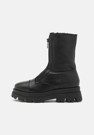 Schwarzer Leder-Mittelschaftstiefel mit grober Profilsohle, abgerundeter Spitze, Reißverschluss vorne und oben sichtbarem Fleecfutter.