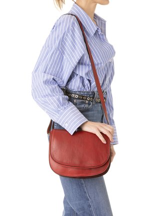 Borsa a tracolla rossa in pelle con una superficie liscia, forma curva e dettagli di cucitura discreti. Indossata sulla spalla, abbinata a una camicia a righe blu.