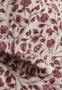 Blumendruckstoff mit einem hellbeigen Hintergrund und tiefburgunderfarbenen Blumen und Blättern, gerafftem Saum und sichtbaren Nähten.