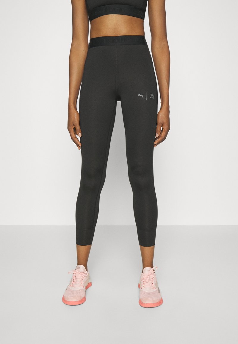 Leggings sportivi neri con un design aderente e lunghezza a metà polpaccio. Presentano un logo Puma e una cintura texturizzata. Indossati con scarpe sportive rosa.