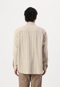 Camisa de rayas beige hecha de tejido ligero, con mangas largas, puños con botones y dobladillo curvado. La vista trasera muestra una textura sutil.