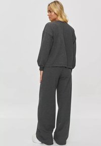 Szary, oversize'owy sweter z opadającymi ramionami i luźnym krojem, w zestawie z szerokimi, szarymi spodniami dresowymi. Miękka tekstura i minimalny design.