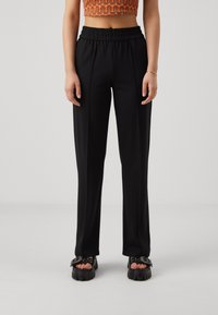 Svarta, högmidjade, skräddarsydda byxor med elastisk midja, med en slät yta och förlängd form, i kombination med kraftiga sandaler.