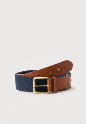Ceinture en tissu bleu avec extrémités en cuir marron et une boucle métallique dorée, avec le nom de la marque GANT embossé sur le cuir.
