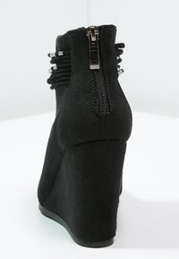 Bottines à talon en forme de coin noires, en matériau suédé doux, avec une fermeture éclair sur le côté et des sangles décoratives autour de la cheville.