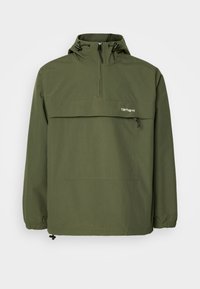 Olivgrüne Anorak-Jacke aus weichem, leichtem Stoff. Mit halbem Reißverschluss, verstellbarer Kapuze und Fronttasche. Mit elastischen Bündchen.