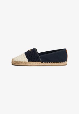Espadrille plate à enfiler avec un dos en tissu bleu marine, un avant tissé noir et blanc texturé et un détail de semelle en jute tressée.