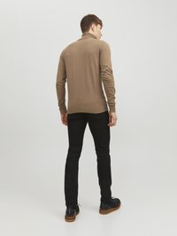 Brauner Langarmpullover mit hohem Kragen, glatter Textur, figurbetontem Stil; kombiniert mit schwarzen Jeans und schwarzen Schuhen mit Holzohr.