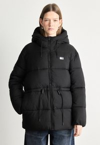 Mustapuffer-takki, jossa on huppu, vetoketjukiinnitys, säädettävät narut vyötäröllä ja pieni logopatch rinnassa.