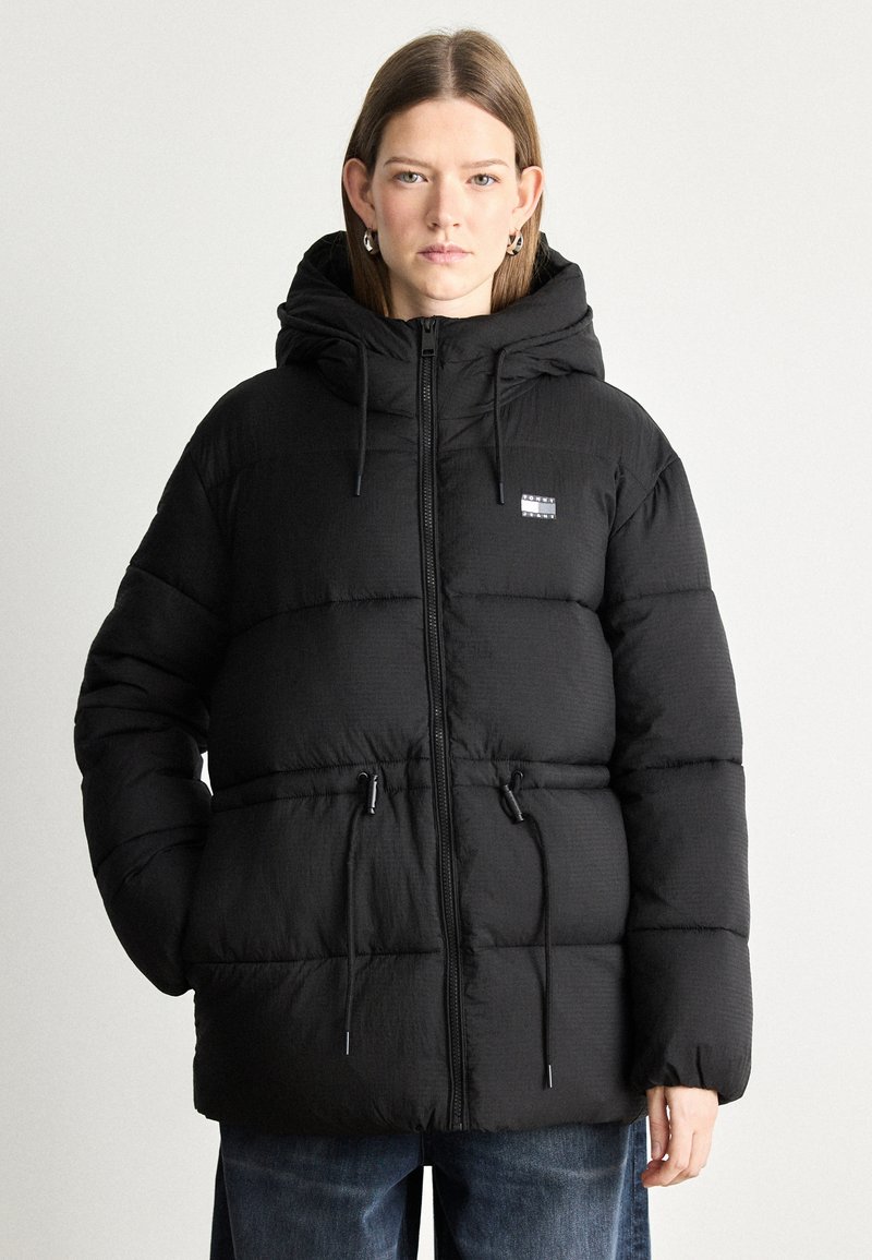 Mustapuffer-takki, jossa on huppu, vetoketjukiinnitys, säädettävät narut vyötäröllä ja pieni logopatch rinnassa.