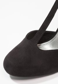 Chaussure plate en daim noir à bout fermé avec bride en T et doublure intérieure argentée, vue en gros plan de face sur fond blanc.