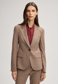 Blazer a scacchi color beige con dettagli rossi, chiusura a un bottone, rever a punta e due tasche frontali, abbinato a una blusa bordeaux.