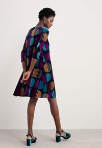 Ein knielanges A-Linien-Kleid in Marineblau mit mehrfarbigen kreisförmigen Mustern in Türkis, Lila und Braun. Es hat Dreiviertelärmel und einen Rundhalsausschnitt.